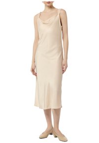 Sukienka na ramiączkach z materiału satynowego w jasnym beżu, z dekoltem w kształcie łódki i cienkimi ramiączkami, sięgająca do połowy łydki, w połączeniu z cielistymi butami na obcasie.