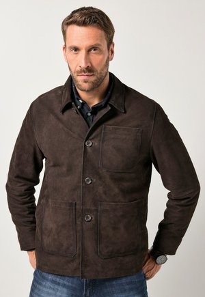Bruine suède jas met een kraag, drie knopen en twee voorzakken. Heeft een zachte textuur en een strakke uitstraling, gecombineerd met denim jeans.