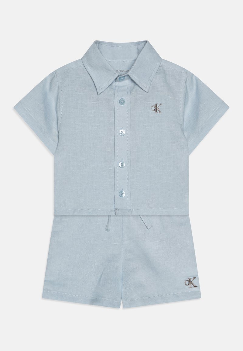 Tenue bleu clair à manches courtes, col, avec fermeture par bouton et ceinture élastique. Présente le logo CK en marron sur la poitrine et à l'ourlet.
