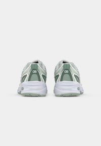 Roheline ja valge New Balance jooksujalanõude paar nähtuna tagant, ühel neutraalsel valgel taustal.