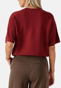 Bordeaux kortærmet sweater med rund hals, tekstureret strik og afslappet pasform, parret med brune skræddersyede bukser med baglommer.