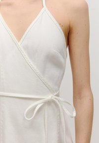Weißes Wickelkleid aus leichtem Stoff, mit tiefem V-Ausschnitt, dünnen Trägern, einer Seitentasche und einem gebundenen Taillendetail.