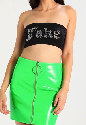 Zwarte strapless top met "Fake" in strassteentjes, gecombineerd met een glanzende groene minirok met hoge taille, voorzien van een rits aan de voorkant en een ringtrekker.