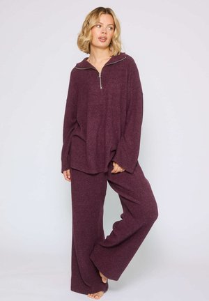 Completo loungewear color marrone con un pullover zip-up rilassato e pantaloni a gamba larga, realizzati in un morbido tessuto strutturato.