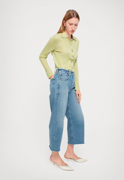 Chemise longue à manches longues de couleur vert clair avec un col et des boutons, associée à un jean en denim bleu à taille haute et ample.