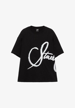 Schwarzes T-Shirt mit kurzen Ärmeln und übergroßem weißen Handschrift-Logo, das teilweise "Staud" auf der Vorderseite buchstabiert.