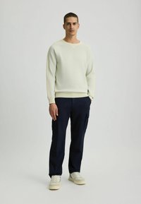  Lichtgele sweatshirt met een ribbeltextuur en V-hals, gecombineerd met marineblauwe cargobroek met zakken en een losse pasvorm. Witte sneakers.