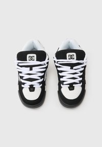 Ténis pretos e brancos com parte superior em tecido, biqueira perfurada, atacadores brancos e sola em borracha. Apresenta um logótipo na lingueta.