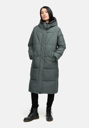 Long, quilted, olive green puffer coat with a hood, featuring side pockets and a straight cut, worn over black pants and boots.
