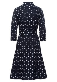 Vestido de lunares en blanco y negro con mangas tres cuartos, cintura ajustada, falda plisada y puños abotonados, visto desde atr�ás.