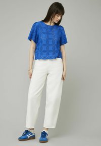 Top en dentelle bleu à motifs avec des manches courtes, ourlet festonné, associé à un pantalon blanc ample et des baskets bleu avec des accents blancs.