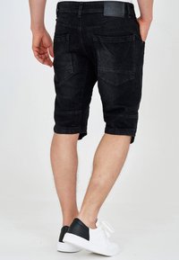 Sorte denimshorts med tætsiddende pasform, knælangt snit og to baglommer. Båret med hvide sneakers med sorte detaljer.