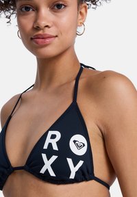 Haut de bikini bleu marine en forme triangulaire, avec lettrage blanc "ROXY" et logo en forme de coeur. Fabriqué en tissu lisse avec bretelles réglables.