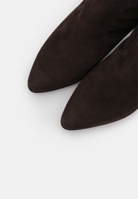 Stivaletti alla caviglia in suede marrone con punta affusolata e inserti elastici laterali, che mostrano una texture liscia su uno sfondo bianco.