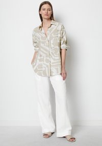 Beige linen shirt with geometric pattern, buttoned front, rolled-up sleeves, paired with white linen wide-leg pants and neutral sandals.