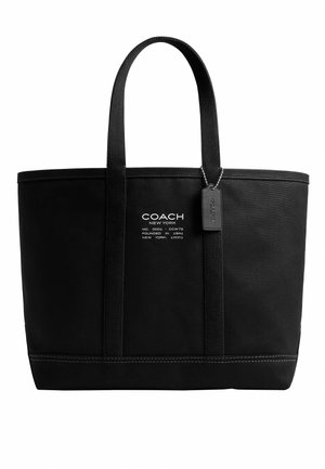 Czarna torba typu tote Coach New York z dwoma uchwytami, białym logo tekstowym i czarną zawieszką na białym tle.