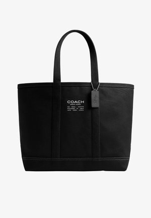 Čierna taška typu tote značky Coach New York s dvoma rukoväťami, bielym textovým logom a visiaci čierny štítok na bielom pozadí.