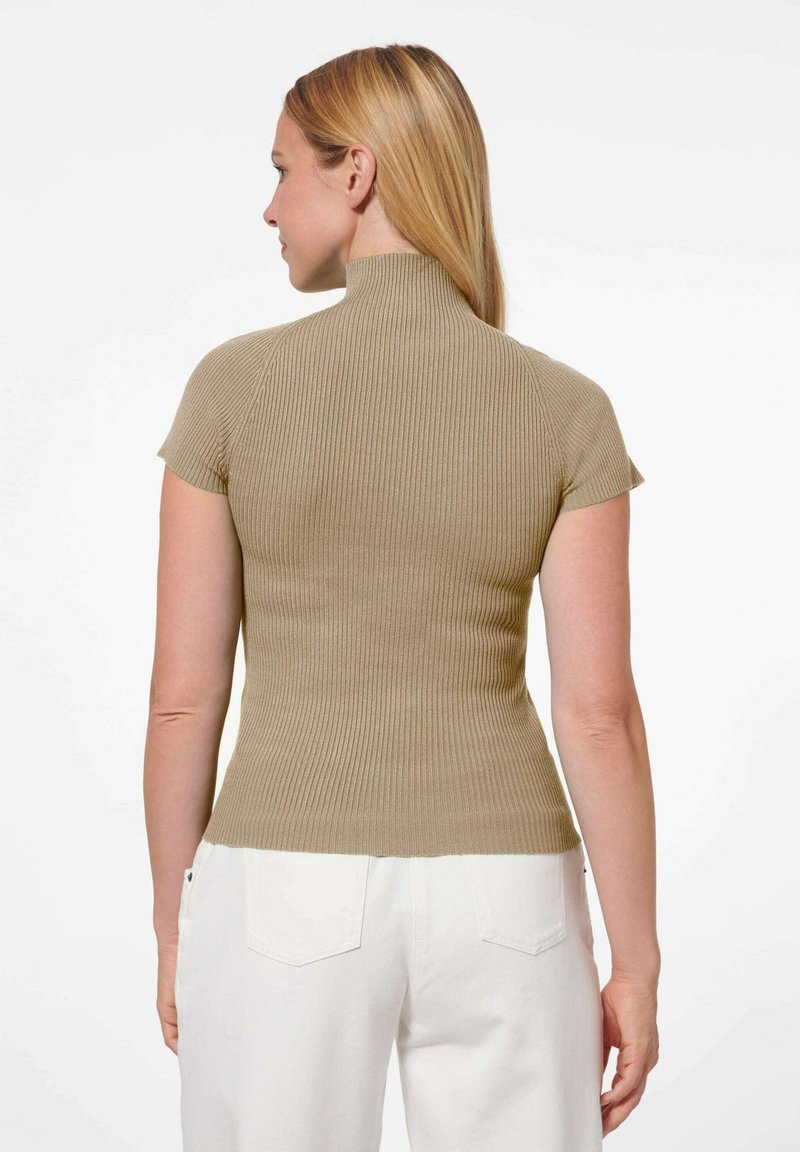 Fitted korte mouw top in beige geribbeld breiwerk, met een hoge nek en een zachte textuur, gecombineerd met witte hoog-was jeans.