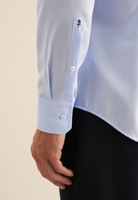 Camicia da uomo di colore azzurro chiaro con una texture liscia, caratterizzata da un design floreale ricamato sul polsino, polsino con bottoni e due bottoni.