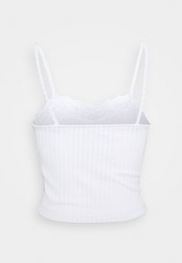 Camisole courte côtelée blanche avec fines bretelles et bordure en dentelle le long du bord supérieur sur un fond uni.