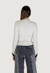 Top blanco de manga larga acanalado con cuello redondo, combinado con jeans de mezclilla gris de talle alto con paneles en contraste y bolsillos traseros.