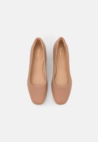 Hnědé syntetické uzavřené lodičky s hladkým povrchem, minimalistickým designem, čtvercovým tvarem a značkovou stélkou, prezentované shora.