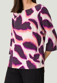 Lila und weiße Bluse mit auffälligen abstrakten Mustern in Pink und Lila. Mit Dreiviertelärmeln und rundem Halsausschnitt. Glatte Stoffoberfläche.