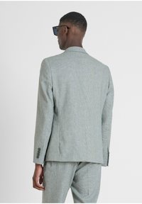 Chaqueta de traje gris claro, texturizada, con una abertura trasera, solapas muesca y puños de cuatro botones, llevada sobre pantalones a juego.