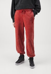 Rote, weiche, strukturierte Sweatpants mit elastischem Bund, Kordelzug und Seitentaschen. Kombiniert mit schwarzen High-Top-Sneakern.