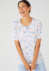 Camiseta de manga corta, blanca, con un patrón floral colorido, que presenta un escote redondo y un pequeño bolsillo en el lado izquierdo. Textura de tela suave.
