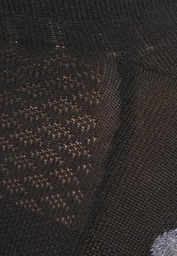 Tessuto di maglia nera con un motivo testurizzato, caratterizzato da densità e tonalità variabili, messo in risalto da riflessi di luce e piccoli contrasti nei dettagli.