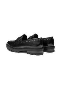 Une paire de mocassins en cuir noir avec des clous le long des bords et des semelles en caoutchouc épais sur fond blanc.