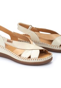 Sandalias de cuero beige con diseño de tiras cruzadas, punta abierta y talón al aire. Presentan costuras en contraste y un tacón cuña bajo.