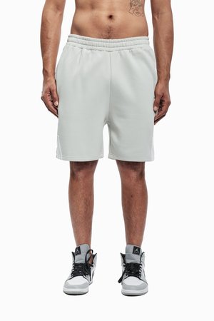 Světlé šedé bavlněné šortky s elastickým pasem, bočními kapsami a decentními švy. Doplňují je černobílé tenisky.