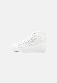 Λευκό ψηλό αθλητικό παπούτσι με πάνελ από δαντέλα, λευκά κορδόνια και λάστιχο σόλα σε απλό ανοιχτό γκρι φόντο.