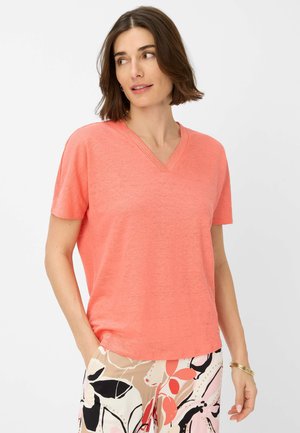 Koralfarvet V-hals T-shirt med korte ærmer, lavet af letvægtsstof. Har subtile syninger ved halsudskæringen, parret med mønstrede bukser.