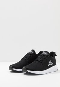 Zwarte sportieve schoenen met een ademende mesh bovenkant, vetersluiting, witte zool en een opvallend wit logo aan de zijkant.