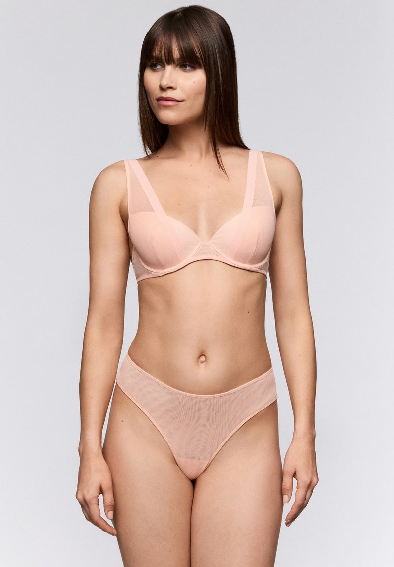 Conjunto de sujetador y tanga de malla en rosa claro con una textura suave. El sujetador tiene tirantes anchos y soporte con aros; el tanga ofrece una cobertura mínima y una cinturilla suave.