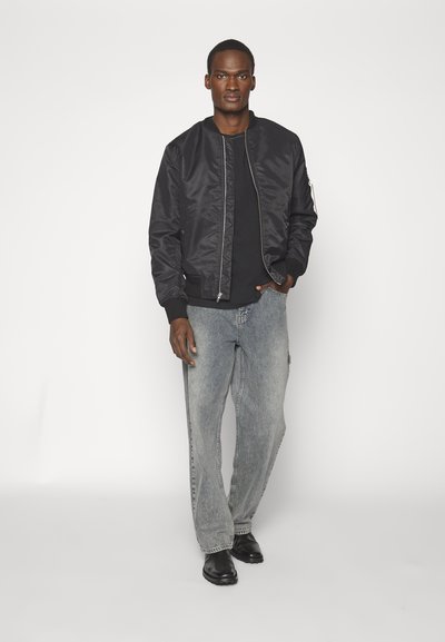 Sort bomberjakke med ribbede manchetter og krave, sammen med falmede blå løstsiddende jeans og sorte læderstøvler. Minimalistisk design.