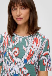 Kolorowa plisowana koszulka z kwiatowym wzorem w odcieniach zieleni, bieli, czerwieni i niebieskiego. Okrągły dekolt i krótkie rękawy. Miękka tekstura.