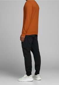 Pull en maille orange, pantalon cargo noir avec poignets élastiques et baskets blanches. La tenue présente une coupe décontractée et un design minimaliste.