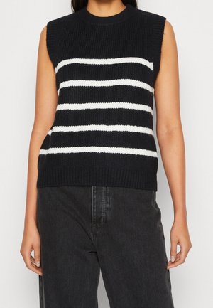 Haut en maille noir sans manches avec quatre bandes blanches horizontales porté avec un jean gris foncé taille haute, visible du cou aux hanches.