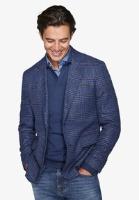 Blazer i blå houndstooth-mønster med klaffelapper og to forlommer, lagd over en navy sweater og denimjeans.