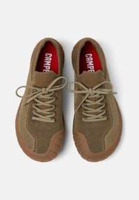 Paire de baskets tricotées marron avec semelles texturées et lacets beige noués en nœuds, semelles intérieures rouges avec le texte blanc « CAMPER ».