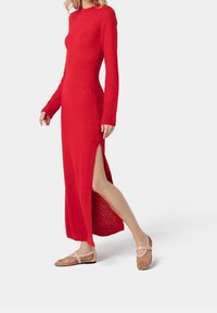 Robe maxi rouge en tricot avec manches longues et fente latérale. Associée à des ballerines en maille beige clair avec une bride. Silhouette simple et ajustée.
