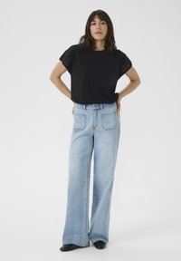 Black short-sleeve top with eyelet detail, paired with light blue wide-leg denim jeans. Smooth fabric, relaxed fit, subtle stitching.