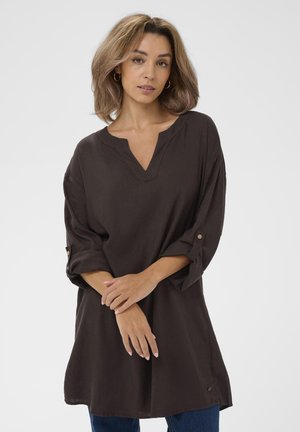 Tunic din in maro cu decolteu în formă de V, mâneci trei sferturi cu accente de buton și o croială lejeră, asociată cu blugi albaștri.