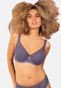 Purple bra featuring sheer panels and lace detailing, with a keyhole accent and adjustable straps. Textured patterns enhance the design.