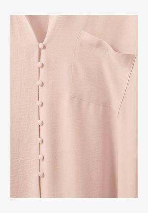 Lyserødt tøj med stofbetrukne knapper i en lodret række og en lille brystlomme på højre side.
