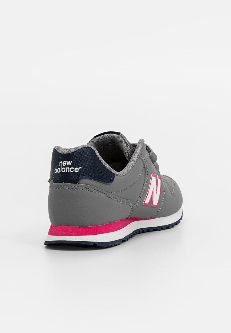 Zapato deportivo gris con una franja rosa, material sintético suave, collar acolchado y logo blanco. Presenta una suela de goma con tracción texturizada.